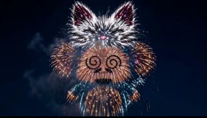 A whimsical nighttime photograph of fireworks arranged to form the shape of a cat's face with glowing eyes, ears, whiskers, and colorful bursts for fur.