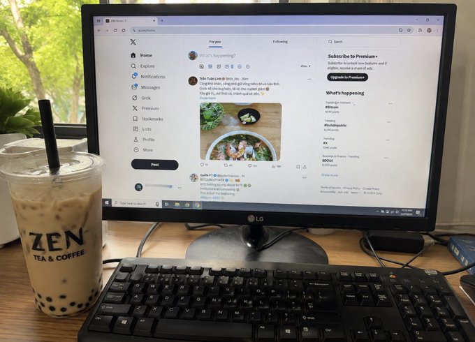 A computer monitor displays the X (formerly Twitter) home feed, with a keyboard in front and a large iced bubble tea from 'ZEN TEA & COFFEE' visible to the left.