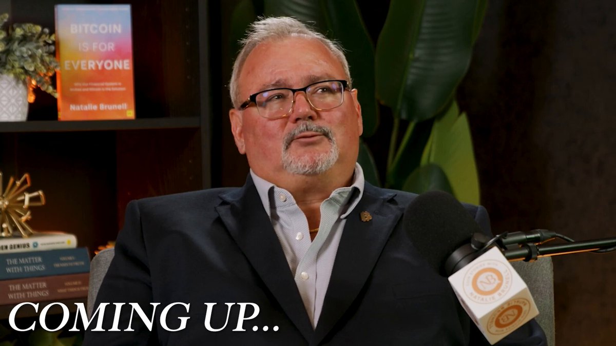 The image features a man wearing glasses sitting in front of a bookshelf filled with various books. The man appears to be talking into a microphone or speaking into an earpiece, suggesting that he might be hosting a podcast or recording an interview. The background includes a potted plant and a vase, adding some greenery and decoration to the scene. The image also contains text that reads "I met Ben Hunnewell at Strategy'S conference and couldn't stop talking to him. He once thought $STRC was too good to be true." This could possibly be an advertisement or promotional material related to Bitcoin or a similar topic, as it seems to feature the man's name and the concept of Bitcoin.