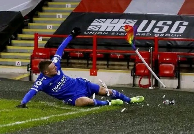 The image features a soccer player wearing blue clothing, who has fallen over while attempting to kick a ball during a game. The player's body is lying on the ground with their legs spread out, indicating that they have lost control of the ball or perhaps twisted their ankle in the process. The scene takes place at a stadium, where there are several chairs and benches visible around the area.