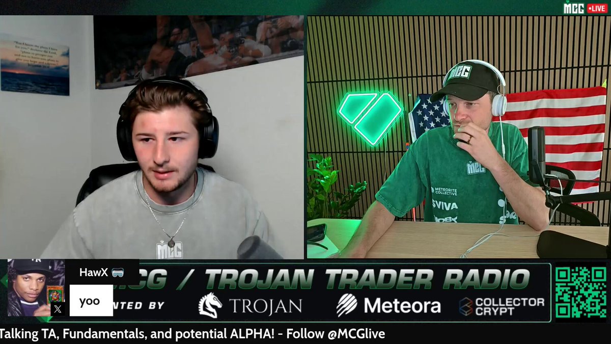 The image depicts two men, one wearing headphones and seated at a desk with a microphone, while the other stands behind him holding a microphone, presumably broadcasting live content or engaging in conversation. The room features an American flag and a poster on the wall, adding to the overall atmosphere of an event or gathering. The background text suggests that these men could be discussing Pokemon and its original sealed packs, as indicated by the "@BedrockFndn's structure" reference present within the image description. This implies that they might be talking about the trading value or significance of the original Pokémon SV151 packs.