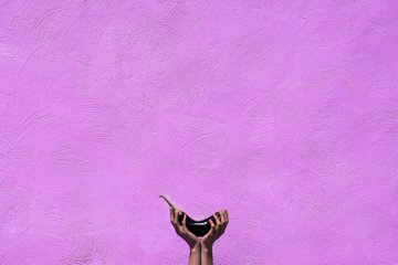 A pair of dark-skinned hands cupped together, holding water against a textured purple background.