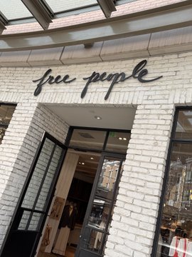The exterior of a Free People store featuring white painted brick walls and black cursive signage above a black-framed entrance.