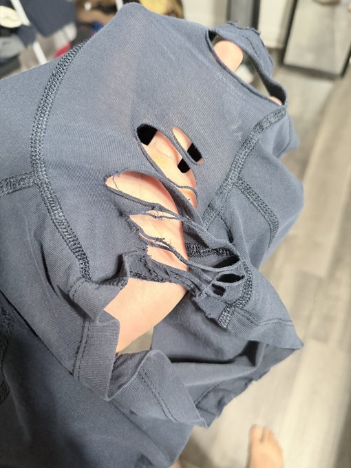 A close-up shot shows a person wearing a distressed dark blue garment with multiple large, frayed cutouts revealing the skin underneath.