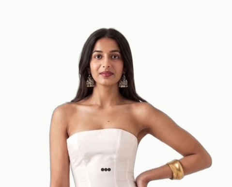 A woman with dark hair poses in a white strapless top and a white skirt with buttons, wearing ornate silver earrings and a gold bracelet.