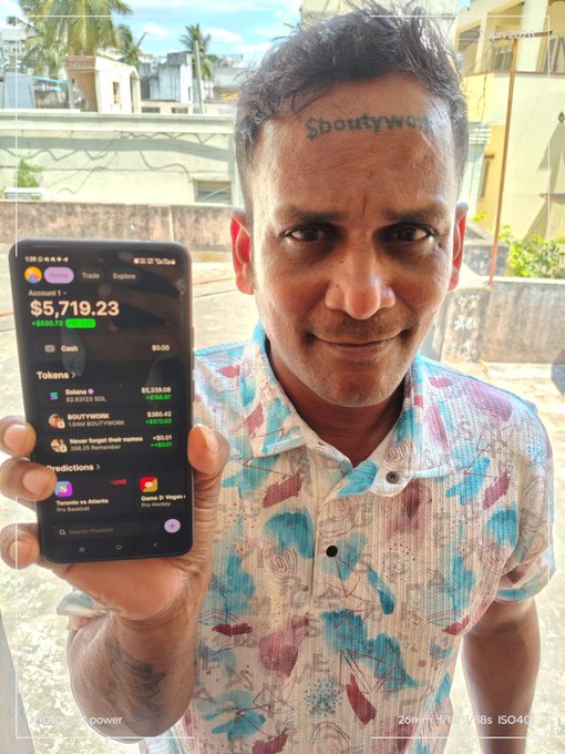 The image features a man holding up his cell phone, displaying its screen. The text "$BOUNTYWORK" can be seen on the phone's display. This suggests that the man might have received an email or message containing this text. The content of the message is not clear from the image alone, but it could potentially be related to a financial topic such as investing in Bitcoin or discussing the value of money.