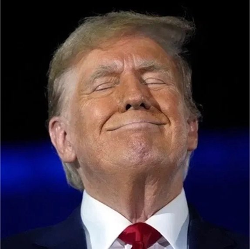 A close-up photo of Donald Trump smiling with his eyes closed, wearing a dark suit and red tie.