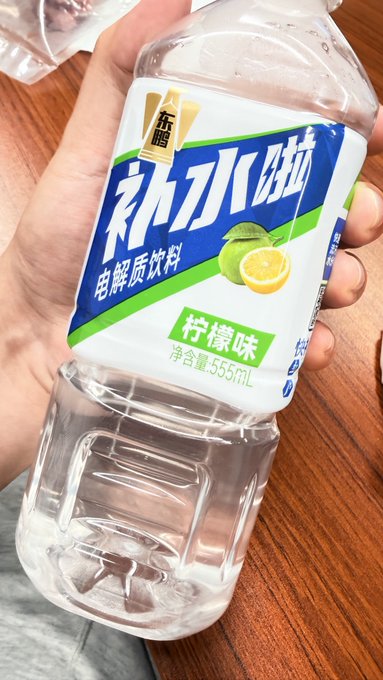 A hand holding a 555mL bottle of Dongpeng (东鹏) electrolyte drink with a lemon flavor label in Chinese.