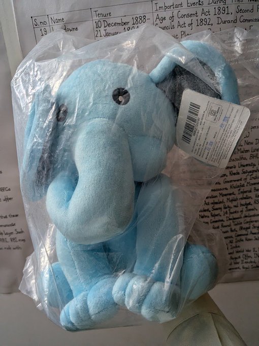 A blue stuffed elephant toy in clear packaging with a visible barcode tag rests on top of a document showing "S.no 19 II," "Name Hema," and tenure dates "10 December 1888-21 January 1907," alongside notes about the "Age of Consent Act 1891" and "Immoral Traffic Act." The image has no direct relation to the post's discussion about Axis Robotics' weighted creator pool system.

The image and caption appear unrelated—the post discusses how Axis Robotics rewards creators through a score-weighted system based on rank, consistency, and referral quality, while the image shows a plush toy displayed on what looks like a historical document about legal tenure and consent acts.