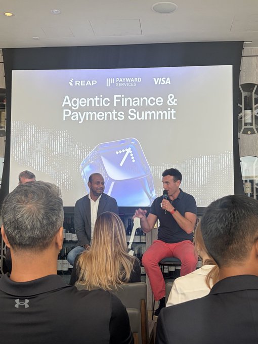 A panel discussion at the 'Agentic Finance & Payments Summit' (co-branded with REAP, Payward Services, and Visa), featuring a man speaking into a microphone while seated next to another man, with an audience visible in the foreground.