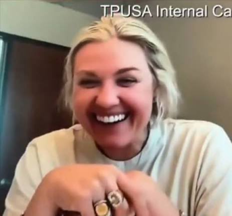 A smiling blonde woman on a video call with the partial text 'TPUSA Internal Ca' visible at the top, wearing a light-colored shirt and rings on her fingers.