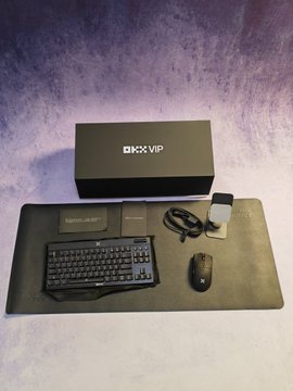 A black DMX VIP subscription box is displayed behind a keyboard, mouse, mousepad, and small accessory box arranged on a desk mat against a purple background.