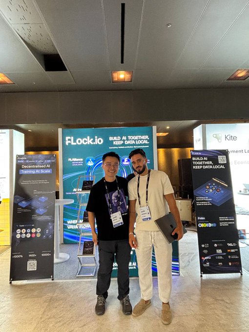 Two men posing for a picture at a tech event, standing in front of a banner that reads 'Flock.io - BUILD AI TOGETHER, KEEP DATA LOCAL' alongside other sponsor displays.