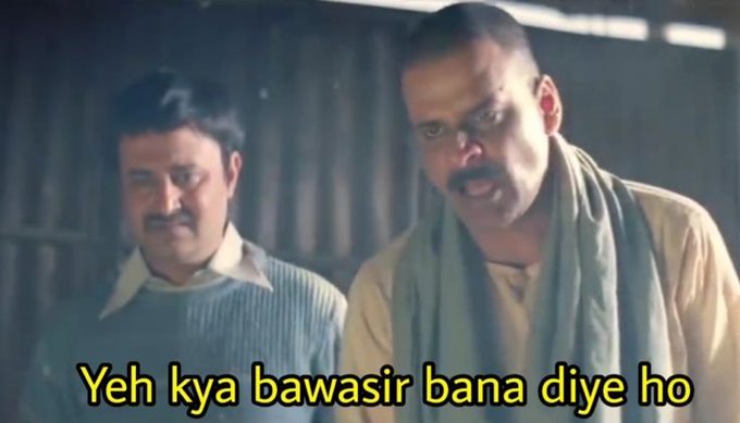 A scene from a Hindi-language film or show showing two men in an interior setting, with the subtitle reading 'Yeh kya bawasir bana diye ho'.