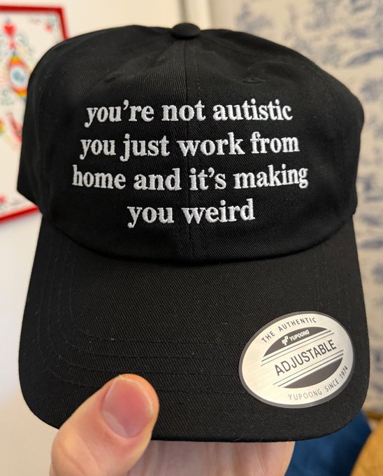 A black baseball cap being held up, featuring white embroidered text that reads 'you're not autistic you just work from home and it's making you weird', with an 'Adjustable YuPoong' sticker on the brim.