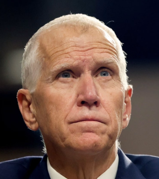 The image shows an older man with white hair and light eyes, looking upward with a serious expression, wearing a dark suit jacket and white collared shirt, appearing to be in an indoor setting with soft lighting. This appears to be Sen. Thom Tillis, whose quote about the Clarity Act's declining odds of approval accompanies the photo, reflecting his concerned expression as he discusses the challenges of passing legislation before the upcoming election.