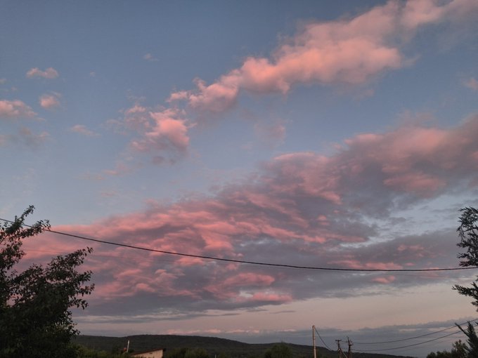 A scenic sunset sky with pink and lavender-tinged clouds over distant hills, with power lines and tree branches visible in the foreground.