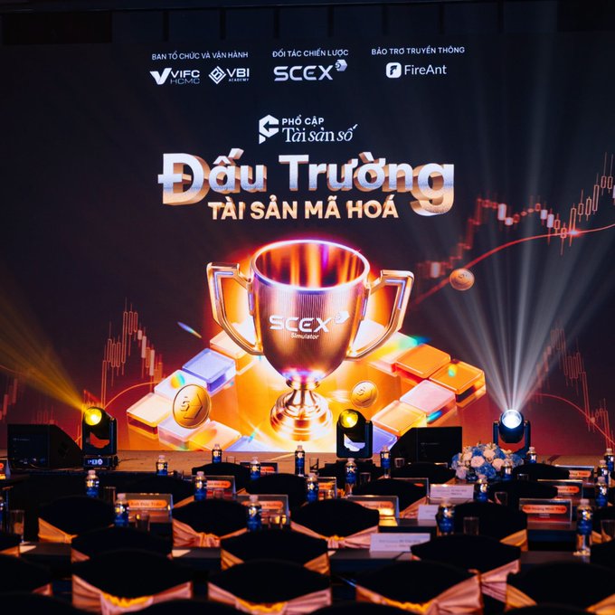 A stage event backdrop displaying 'Đấu Trường Tài Sản Mã Hoá' (Crypto Asset Arena) by SCEX Simulator, featuring a large trophy graphic and sponsor logos including VIFC, VBI, and FireAnt.