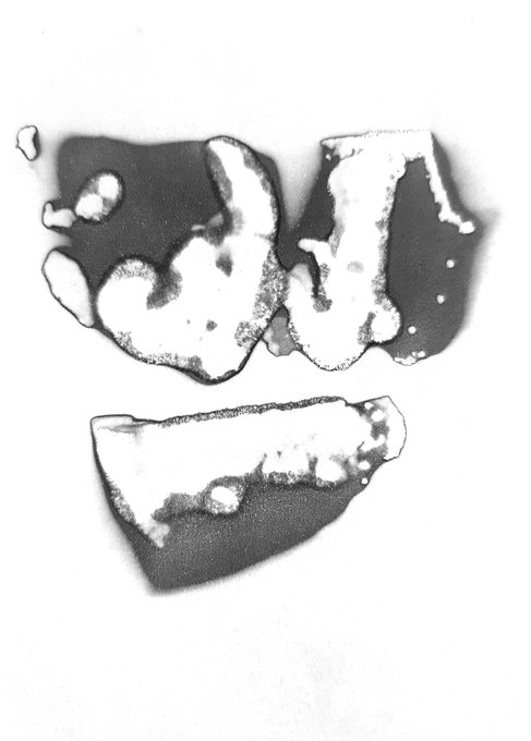 A black and white abstract inkblot or Rorschach-style image featuring symmetrical dark shapes resembling a crown or fragmented form on a white background.
