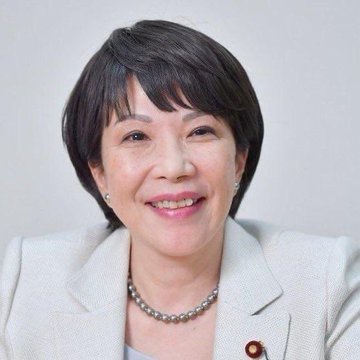 The image features a woman with short hair wearing a white blazer jacket. She has a smile on her face as she looks directly at the camera. The background of the photo is plain white, which makes the woman stand out even more. There are no other objects or people in the image besides the woman and the background.