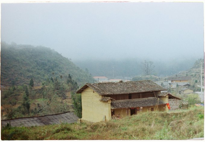 The image shows an old yellow house with a sloping roof, situated at the bottom of a hill surrounded by trees. The sky above appears hazy, suggesting that the photo was taken during a cloudy day or early morning hours. The house is located in a rural area and seems to be part of a larger landscape. The post about AI projects and blockchain updates has been shared on social media platforms, reaching a wide audience.