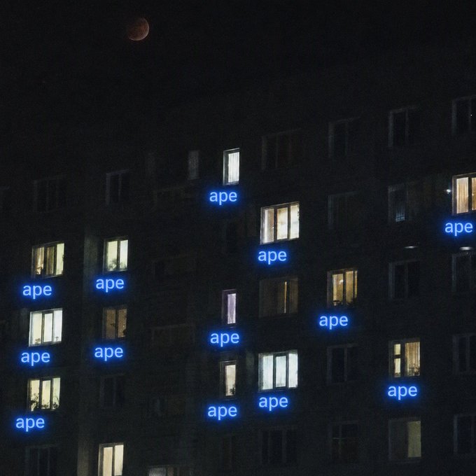A nighttime photo of an apartment building with illuminated windows, overlaid with the word "ape" glowing in blue neon in multiple windows, and a blood-red moon in the upper left corner. The image reflects the post's bullish $APE sentiment, symbolizing the token's dominance among "degens" over the long weekend, with the red moon hinting at a "blood moon" market moment.