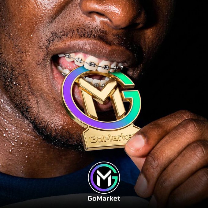 A close-up photograph of a man with braces holding a gold and multicolored 'GoMarket' medal/charm in his mouth, with the GoMarket logo visible at the bottom.
