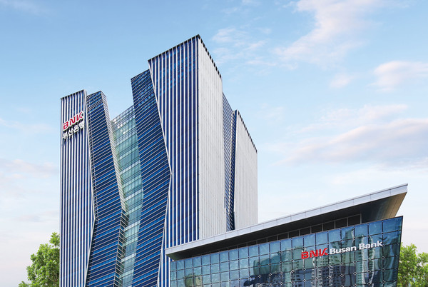 A modern glass skyscraper with the BNK Busan Bank logo displayed on both the high-rise tower and the lower building in the foreground.