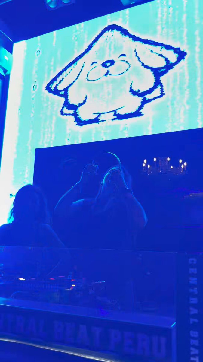 The image features a DJ booth with a large screen displaying a cartoon dog logo, likely representing a popular music artist or band. The background of the image shows a person standing behind the DJ booth, possibly preparing for their performance. The caption at the bottom of the photo reads "Central Beat Peru".