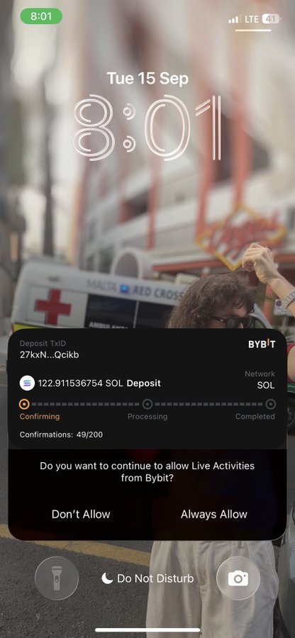 An iPhone lock screen showing the time 8:01 on Tue 15 Sep, with a Bybit deposit notification for SOL tokens over a blurred background of a street parade.