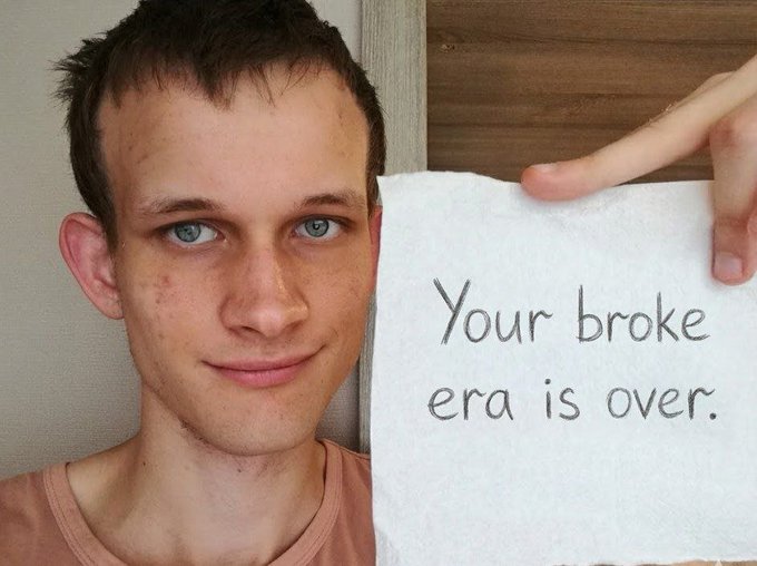 A young man with a receding hairline holds up a piece of paper with handwritten text reading 'Your broke era is over.'