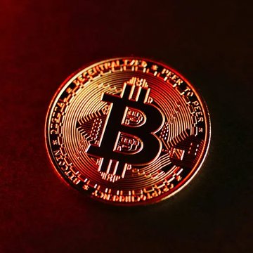 A golden Bitcoin (₿) token glows against a dark red background, symbolizing the cryptocurrency market's tension. The image reinforces the post's "PRICE ALERT" about a -$6.3K Bitcoin drop coinciding with the US government transferring $BTC and $WBTC to Coinbase Prime, visually evoking the alarm and volatility of the event.