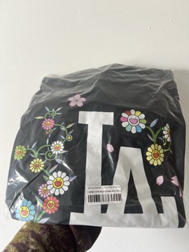 A black LA Dodgers cap decorated with colorful floral designs, sealed in clear plastic packaging with a visible barcode tag.
