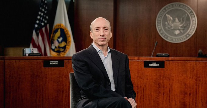 The image shows a man sitting in a chair, possibly in a courtroom or an office setting. The man appears to be balding with a serious expression as he looks directly at the camera. In front of him are two flags - one representing the United States and another symbolizing Ripple cryptocurrency. There is also a post on this image that questions whether Gary Gensler was right about Ripple being a scam, suggesting an ongoing debate or discussion related to the cryptocurrency market.
