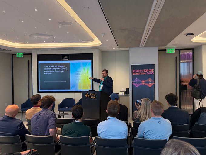 A conference room where a speaker presents on 'Cryptographically Relevant Quantum Computers (CRQCs)' at a Converge Boston DAO event, with a Folly Hoag podium visible.