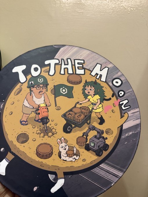 A circular cartoon illustration titled 'TO THE MOON' depicting characters mining cryptocurrency on a moon-like surface with coins, a jackhammer, a flag, and a small robot.