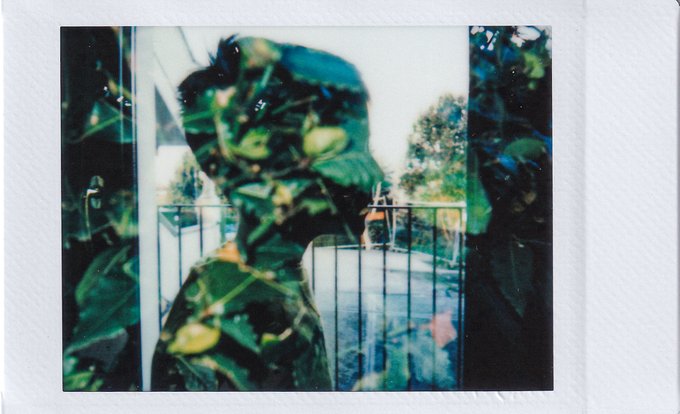 A Polaroid-style photograph showing a person wearing a helmet, with the image overlaid by green foliage creating a double-exposure effect against a blurred background.