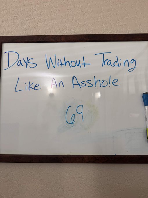 Whiteboard in an office with the handwritten message 'Days Without Trading Like An Asshole' and the number '69' written below it in blue marker.