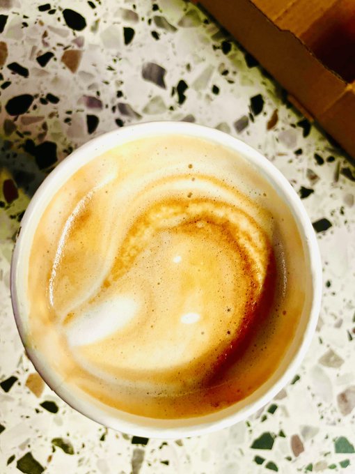 A top-down view of a cup of coffee with swirled latte art, sitting on a terrazzo speckled table.