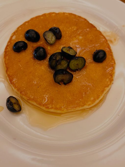A stack of pancakes topped with sliced blueberries and syrup, served on a white plate.