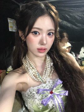 A young woman wearing a pearl necklace and an ornate white and green dress, looking at the camera.