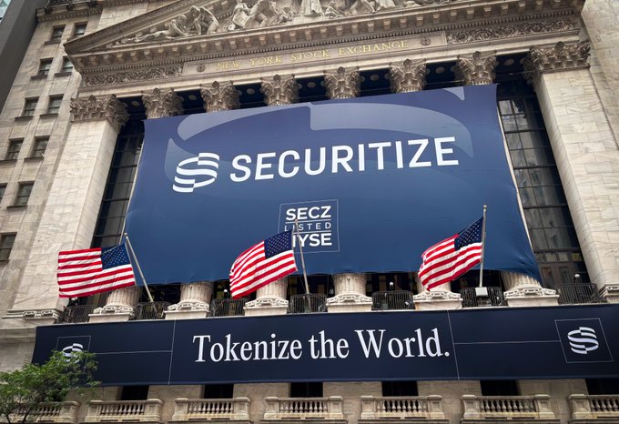 A large banner on the New York Stock Exchange building displays "SECURITIZE" with "SECZ LISTED NYSE" and the tagline "Tokenize the World," celebrating the company's NYSE listing under ticker SECZ in alignment with the post's announcement of tokenization's day at the NYSE.