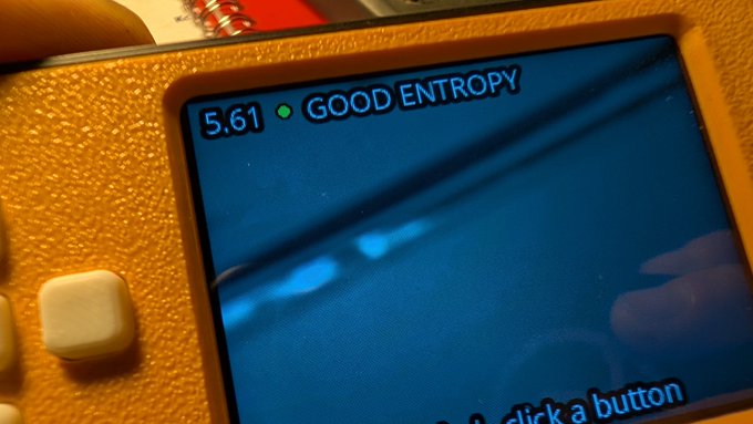 A close-up of a SeedSigner's LCD screen displays "5.61 GOOD ENTROPY" with a green indicator light, confirming the device successfully generated strong cryptographic randomness for Bitcoin seed creation. The partially visible text "...pick a button" at the bottom suggests the user is interacting with the device's interface to proceed.