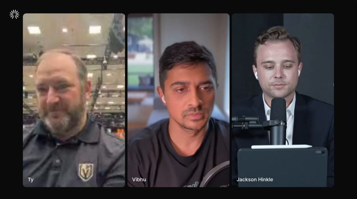 The image shows three men sitting at a table with microphones in front of them, likely participating in an online video call or webinar. The man on the left side of the screen has a beard and is wearing a black shirt. In the middle, there's another man who appears to be balding. On the right side of the image, you can see a third person with short hair sitting at the table. The background features a wall that is painted white, providing a neutral backdrop for the three men in focus.