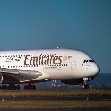 A large Emirates Airbus A380 aircraft landing or taking off, displaying the airline's branding and 'www.emirates.com' on the fuselage.