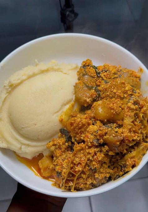 A white bowl filled with a yellow mashed food (likely fufu or banku) alongside a reddish-orange stew with meat, vegetables, and spices.