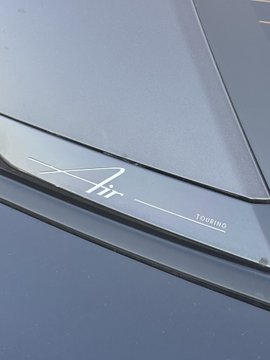 A close-up of a dark blue car's rear badge with script text 'Air' and 'TOURING'.