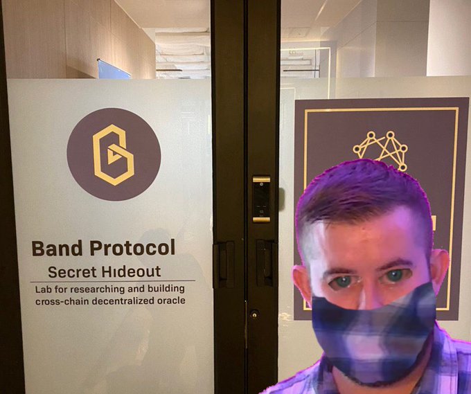 A person's selfie in front of a 'Band Protocol Secret Hideout' office door with the 'Lab for researching and building cross-chain decentralized oracle' tagline and the Band Protocol logo.