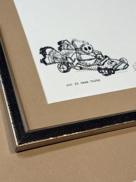 A close-up of a framed art print depicting a whimsical raccoon cartoon, with text beneath reading 'Jan 14 Seek Turtle'.