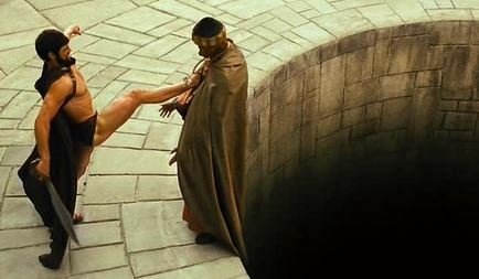 A scene from a movie showing two gladiators fighting on a stone platform above a dark pit, with one man kicking the other.
